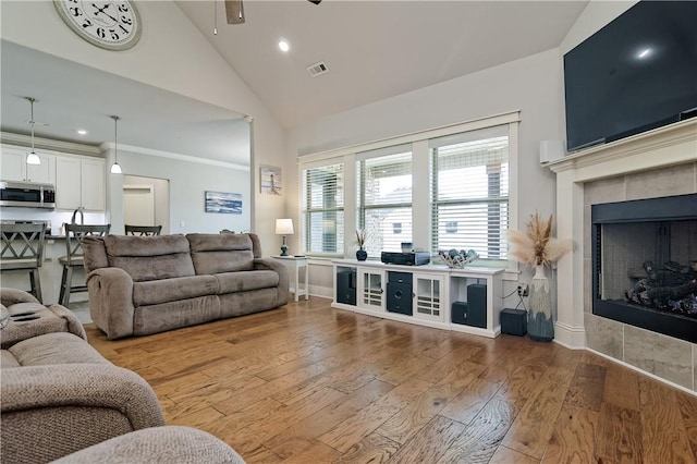 living room featuring hardwood / wood-style flooring, a tile fireplace, and high vaulted ceiling