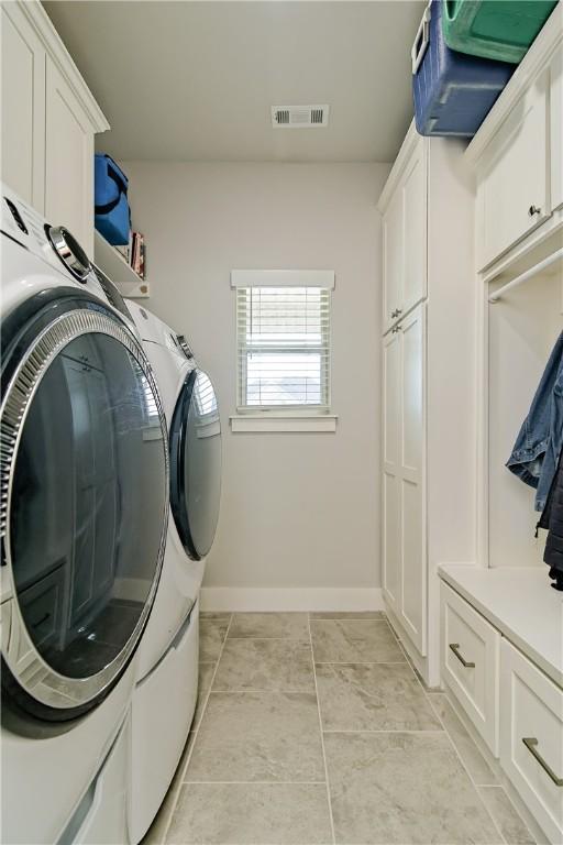 washroom featuring washing machine and dryer, light tile patterned floors, and cabinets