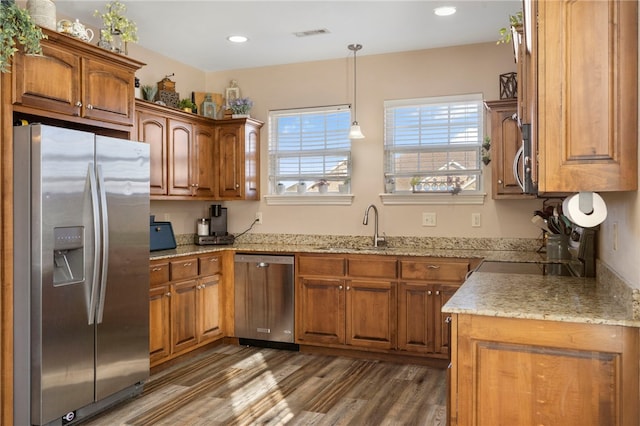 kitchen featuring appliances with stainless steel finishes, sink, decorative light fixtures, dark wood-type flooring, and light stone counters