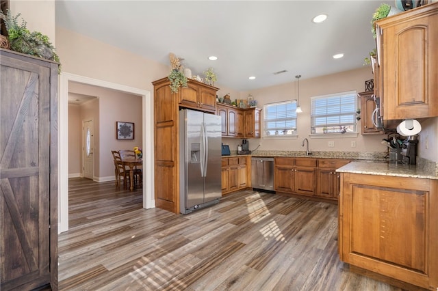 kitchen with light stone counters, hardwood / wood-style floors, stainless steel appliances, and pendant lighting