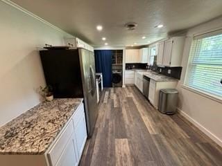 kitchen featuring light stone countertops, appliances with stainless steel finishes, white cabinetry, dark hardwood / wood-style floors, and ornamental molding