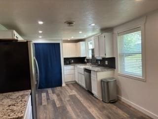 kitchen featuring white cabinetry, light stone counters, appliances with stainless steel finishes, and wood-type flooring