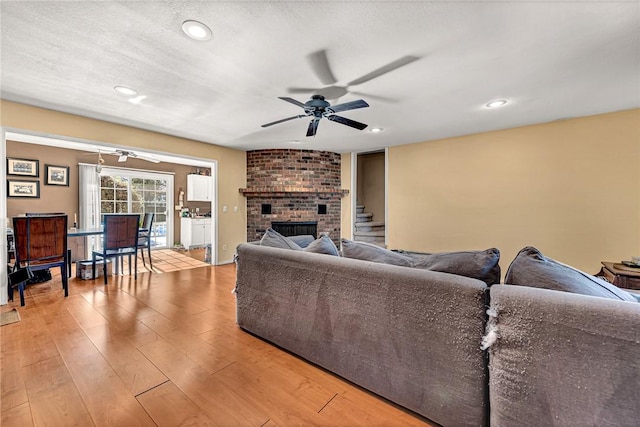 living room featuring ceiling fan, a textured ceiling, light wood-type flooring, and a fireplace