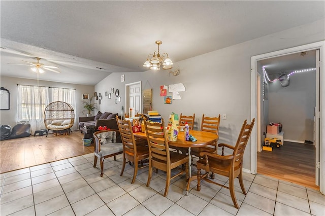 tiled dining room with ceiling fan with notable chandelier and vaulted ceiling