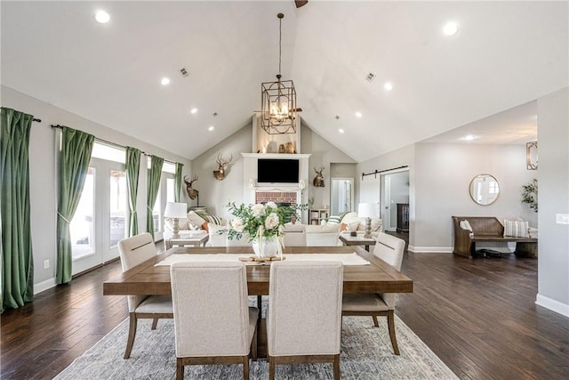 dining area with dark wood-type flooring, an inviting chandelier, a barn door, and high vaulted ceiling