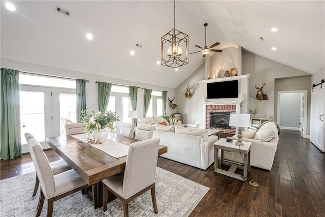 dining room with ceiling fan, high vaulted ceiling, a fireplace, dark hardwood / wood-style flooring, and a barn door