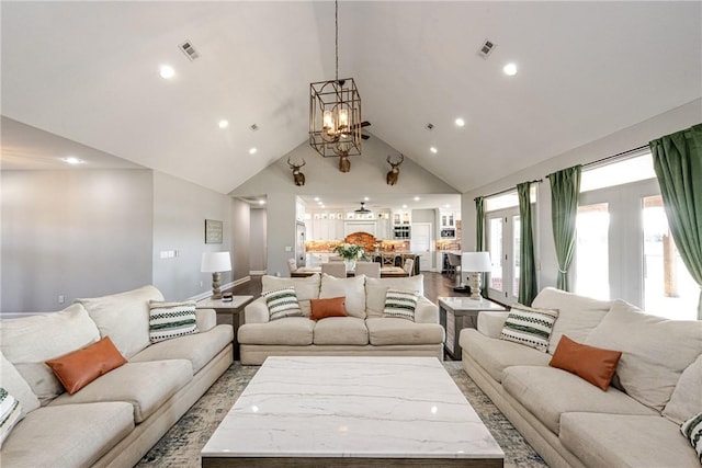 living room with high vaulted ceiling, an inviting chandelier, and light hardwood / wood-style floors