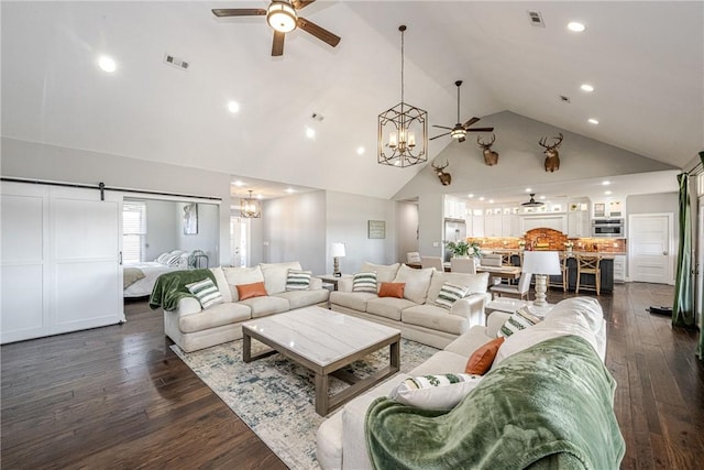 living room featuring ceiling fan with notable chandelier, dark hardwood / wood-style floors, high vaulted ceiling, and a barn door