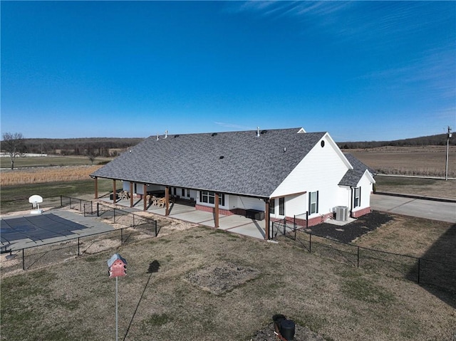 rear view of property featuring a rural view, central AC, a patio, and a lawn