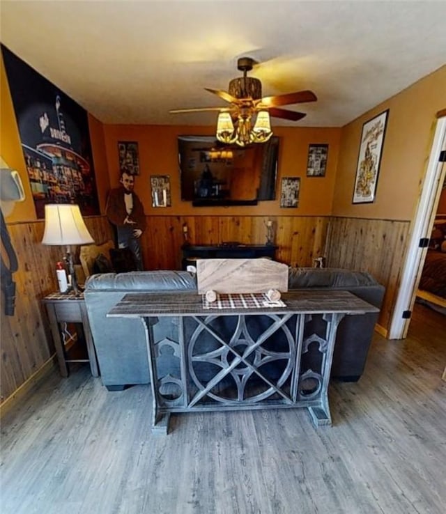 living room featuring hardwood / wood-style flooring, wooden walls, and ceiling fan