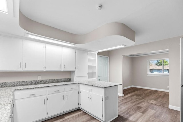 kitchen featuring kitchen peninsula, hardwood / wood-style floors, white cabinets, and light stone counters