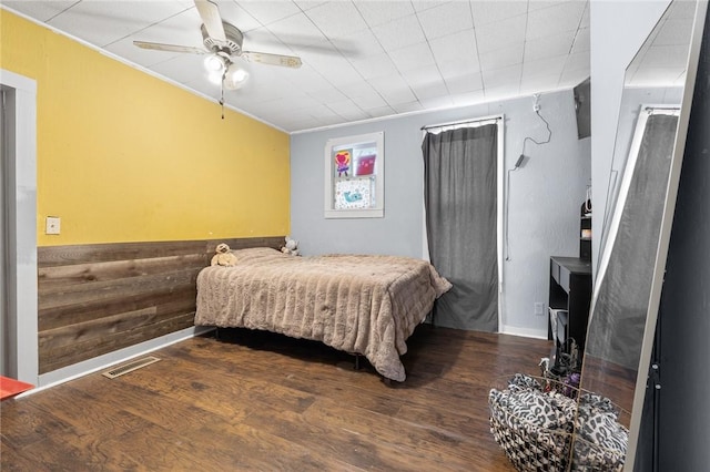 bedroom with ceiling fan, wood walls, and wood-type flooring