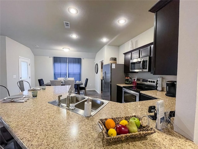 kitchen with appliances with stainless steel finishes, sink, dark brown cabinetry, kitchen peninsula, and a breakfast bar area