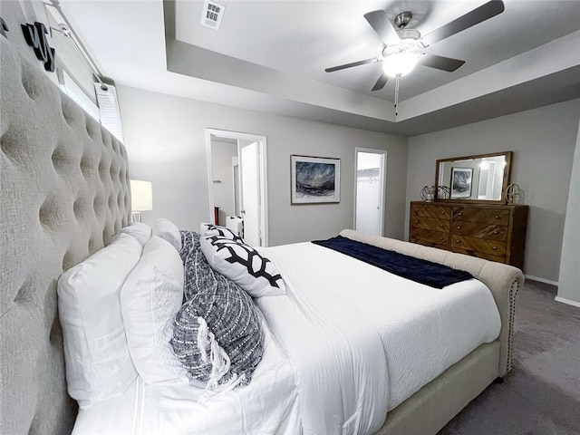 bedroom with ceiling fan, connected bathroom, carpet floors, and a tray ceiling