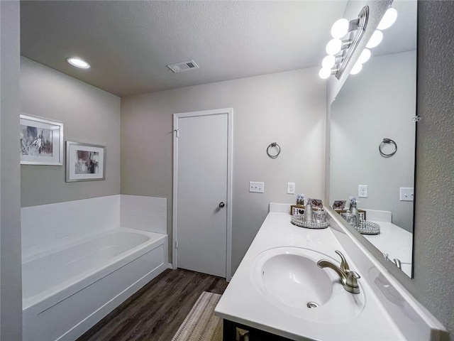 bathroom with wood-type flooring, a textured ceiling, a bathtub, and vanity