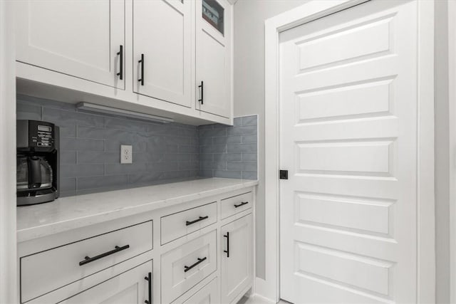 bar with decorative backsplash, light stone countertops, and white cabinetry