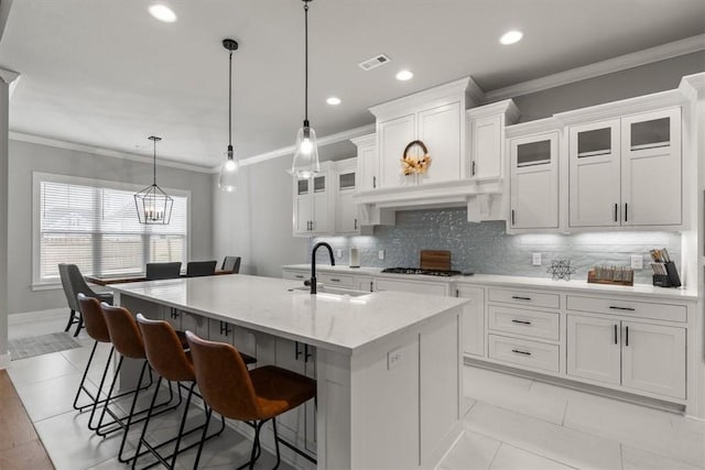 kitchen with white cabinetry, a kitchen island with sink, pendant lighting, a breakfast bar, and light stone counters