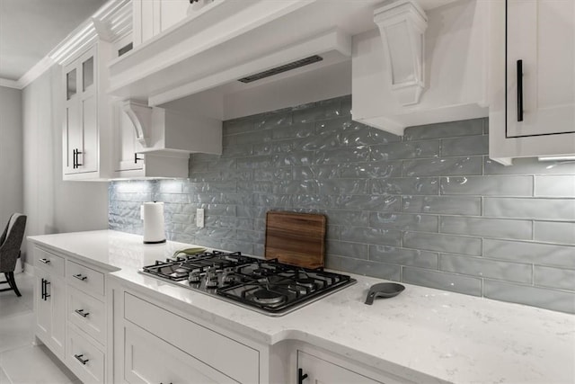 kitchen with light stone countertops, backsplash, white cabinets, and stainless steel gas cooktop