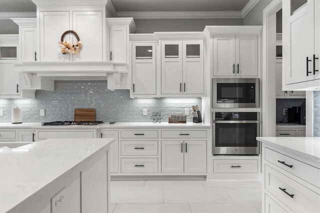 kitchen with crown molding, backsplash, white cabinets, light stone counters, and stainless steel appliances