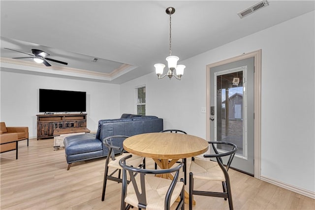 dining room featuring ceiling fan with notable chandelier, a wealth of natural light, a tray ceiling, and light hardwood / wood-style flooring