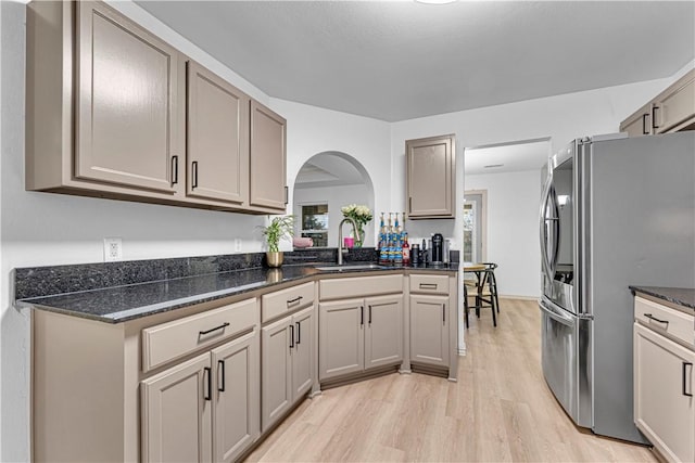 kitchen featuring sink, dark stone countertops, light wood-type flooring, and stainless steel fridge