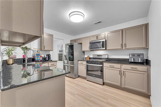 kitchen featuring kitchen peninsula, light hardwood / wood-style flooring, sink, dark stone counters, and stainless steel appliances