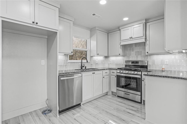 kitchen featuring sink, stainless steel appliances, dark stone countertops, and white cabinetry