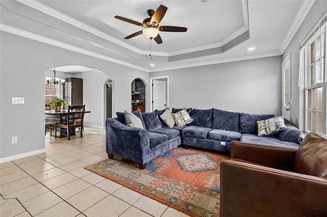 tiled living room with ornamental molding, a tray ceiling, and ceiling fan with notable chandelier