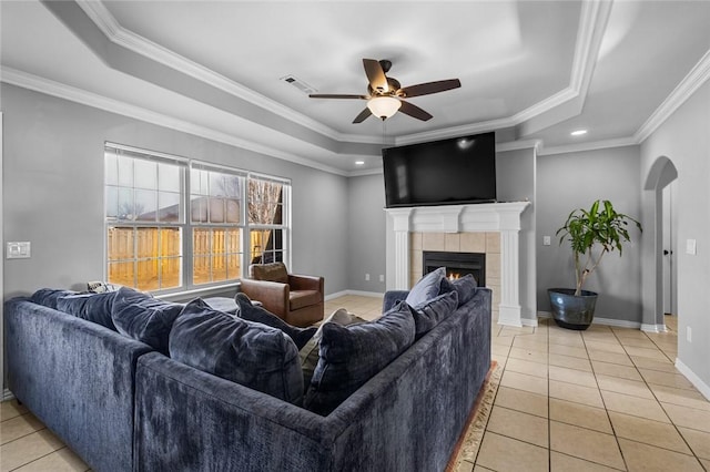 living room with a raised ceiling, crown molding, and a tiled fireplace