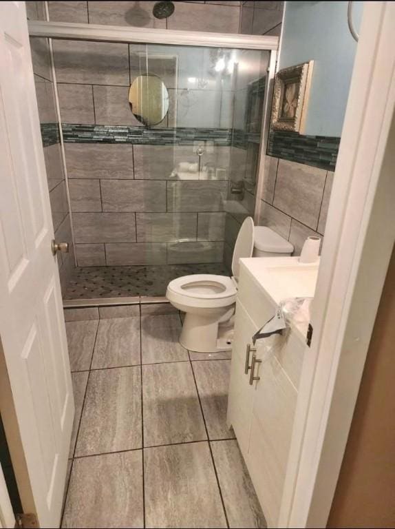 bathroom featuring tile walls, tile patterned flooring, vanity, walk in shower, and toilet