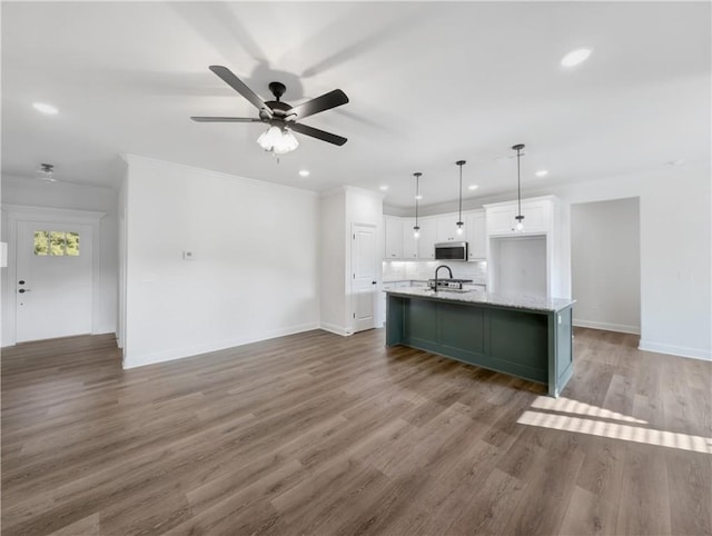 kitchen featuring dark hardwood / wood-style floors, decorative light fixtures, white cabinetry, backsplash, and a center island with sink