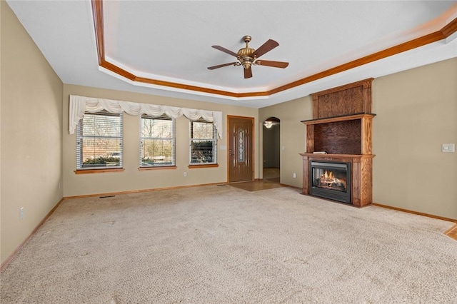 unfurnished living room featuring light carpet, a tray ceiling, a large fireplace, and ceiling fan