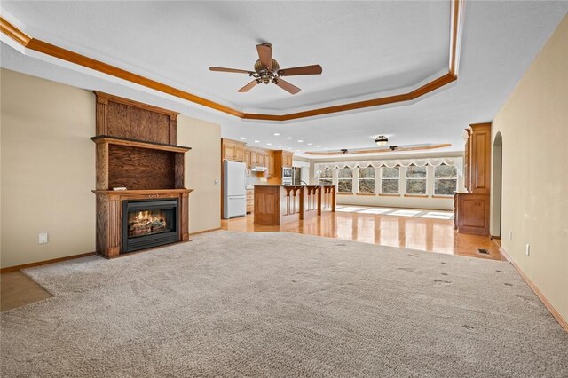 unfurnished living room with a tray ceiling, light colored carpet, and a large fireplace