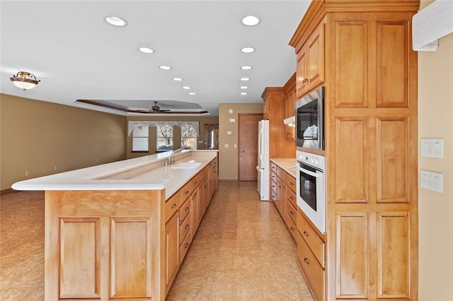 kitchen featuring ceiling fan, sink, an island with sink, and white appliances