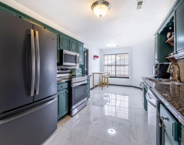 kitchen featuring appliances with stainless steel finishes, sink, a textured ceiling, and dark stone countertops