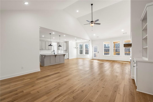 unfurnished living room featuring high vaulted ceiling, sink, ceiling fan, and light hardwood / wood-style flooring