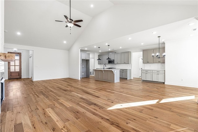 unfurnished living room with visible vents, baseboards, high vaulted ceiling, light wood-style flooring, and ceiling fan with notable chandelier