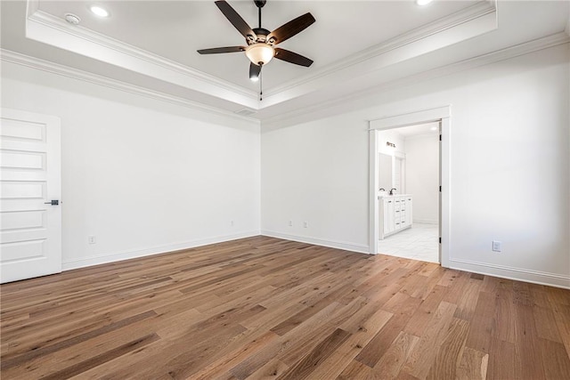 unfurnished room featuring a raised ceiling, wood finished floors, baseboards, and ornamental molding