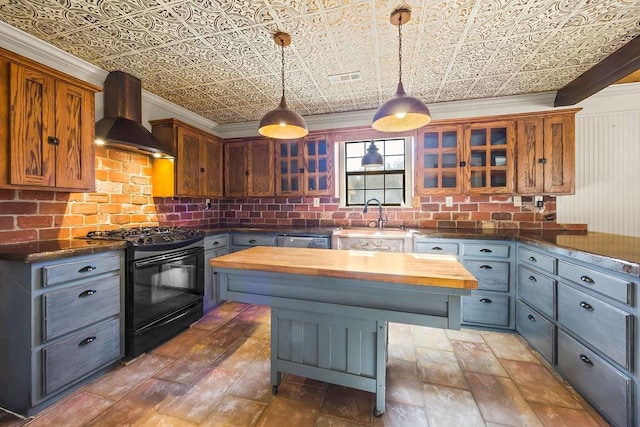 kitchen with pendant lighting, black range with gas cooktop, sink, wooden counters, and wall chimney exhaust hood