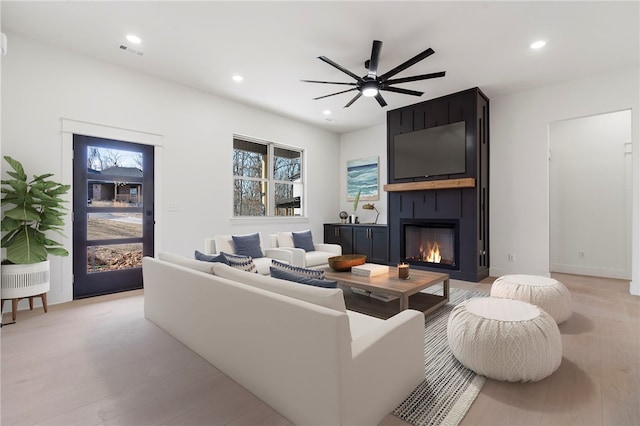 living room featuring ceiling fan, a large fireplace, and light wood-type flooring