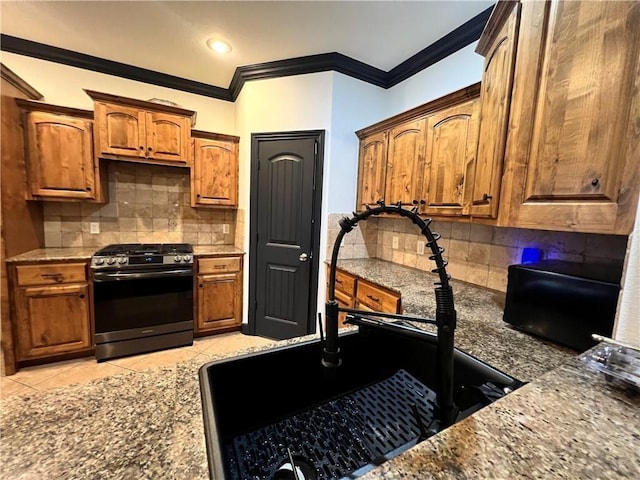 kitchen featuring backsplash, light tile patterned floors, stainless steel range with gas cooktop, and sink