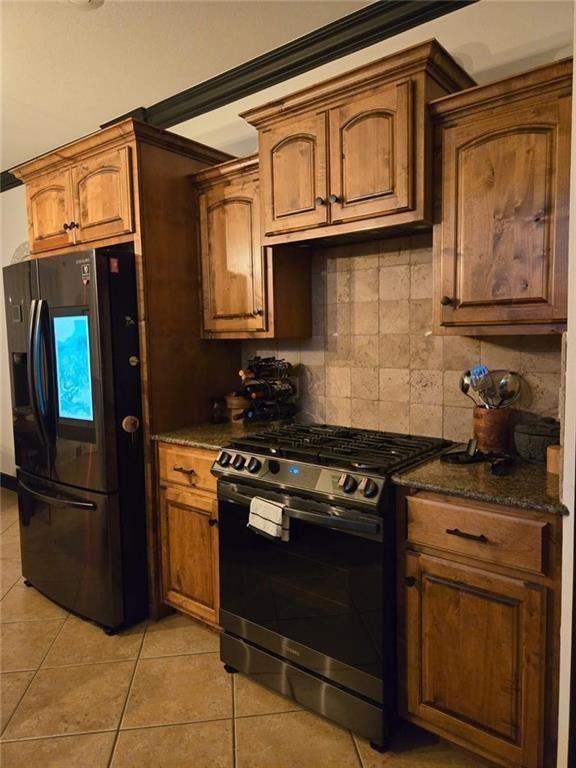 kitchen featuring light tile patterned floors, stainless steel gas range, dark stone countertops, tasteful backsplash, and black fridge