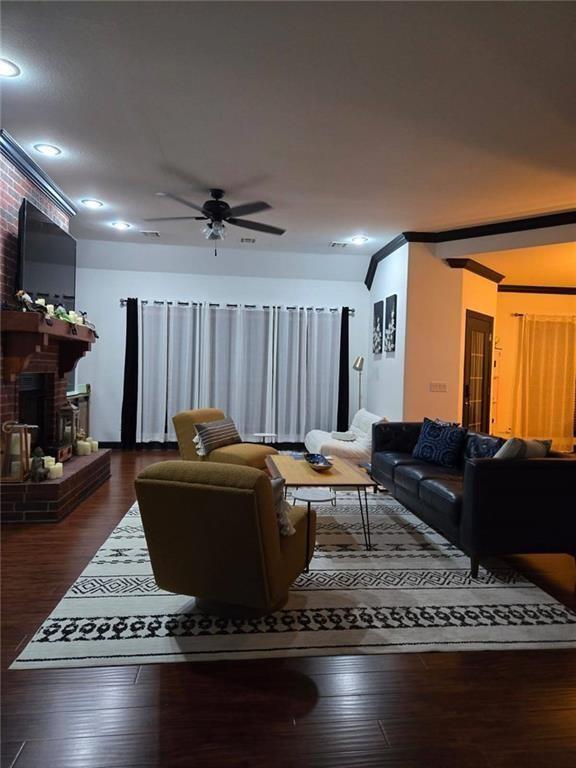 living room with a brick fireplace, dark hardwood / wood-style floors, and ceiling fan