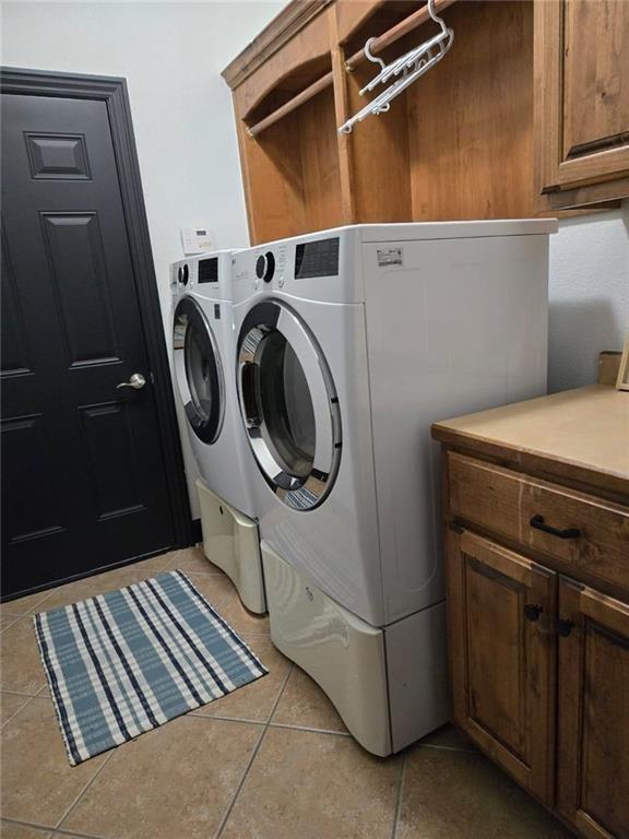 clothes washing area with separate washer and dryer, cabinets, and light tile patterned flooring