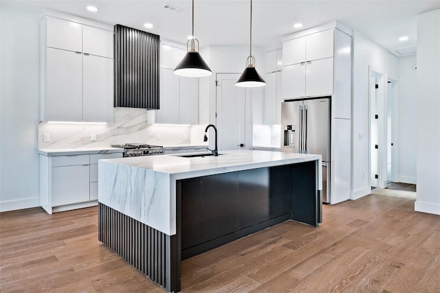 kitchen with white cabinetry, sink, high quality fridge, and a center island with sink