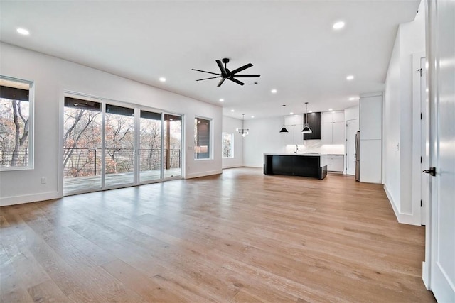 unfurnished living room with ceiling fan, sink, and light wood-type flooring