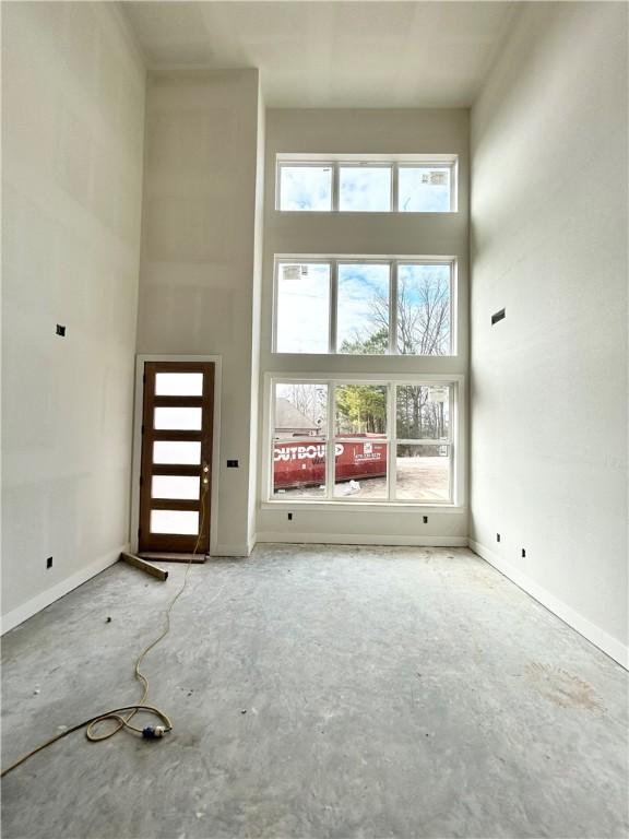 unfurnished living room with concrete flooring, a healthy amount of sunlight, and a high ceiling