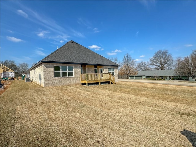 rear view of house featuring brick siding, central air condition unit, roof with shingles, a yard, and a deck