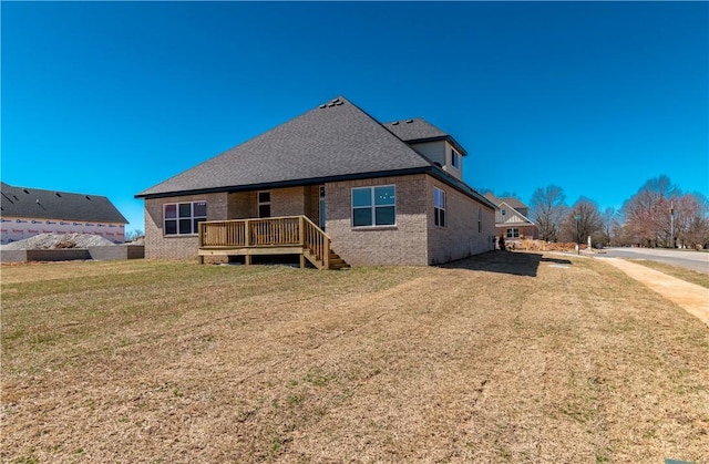 rear view of property featuring brick siding, roof with shingles, and a lawn