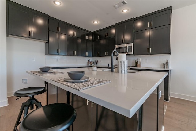 kitchen with tasteful backsplash, visible vents, stainless steel microwave, and dark cabinets